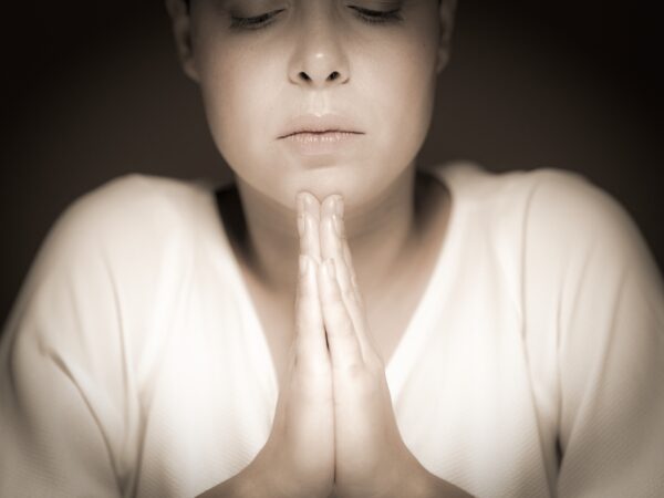 mulher rezando com roupa branca num fundo preto