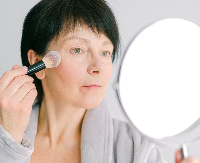 mulher de 50 anos em frente ao espelho fazendo maquiagem