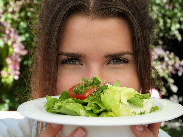 mulher morena mostrando um prato com salada verde