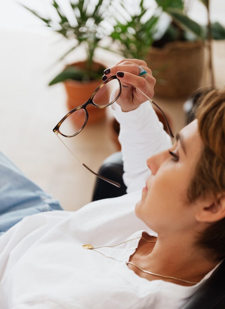 mulher de branco sentada de costas com óculos na mão