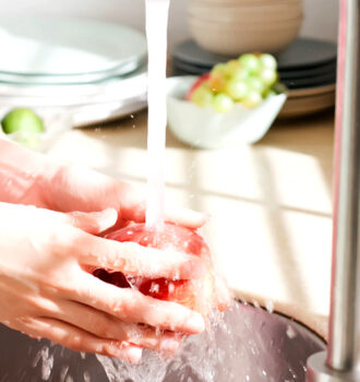 mãos embaixo de uma torneira higienizando uma fruta