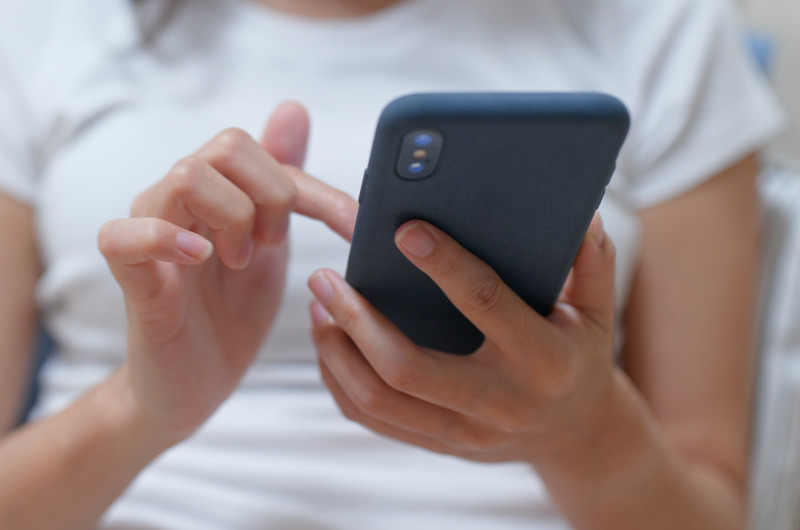 Mulher de camisa branca segurando um celular preto