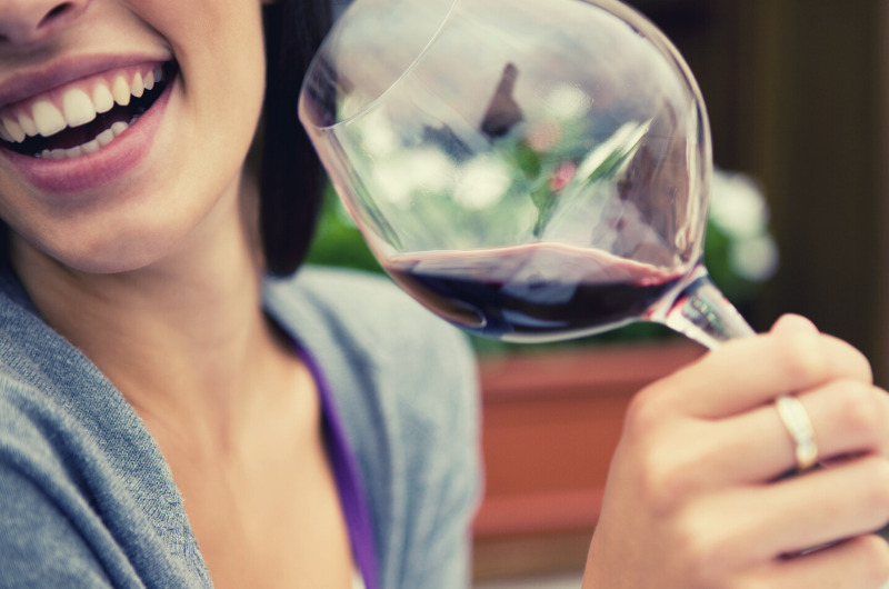 mulher sorrindo segurando uma taça com vinho tinto